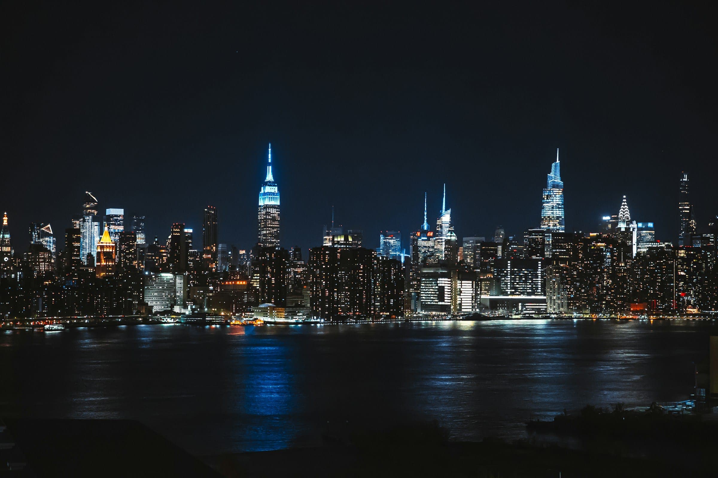 A city skyline at night, lit windows reflected in the water